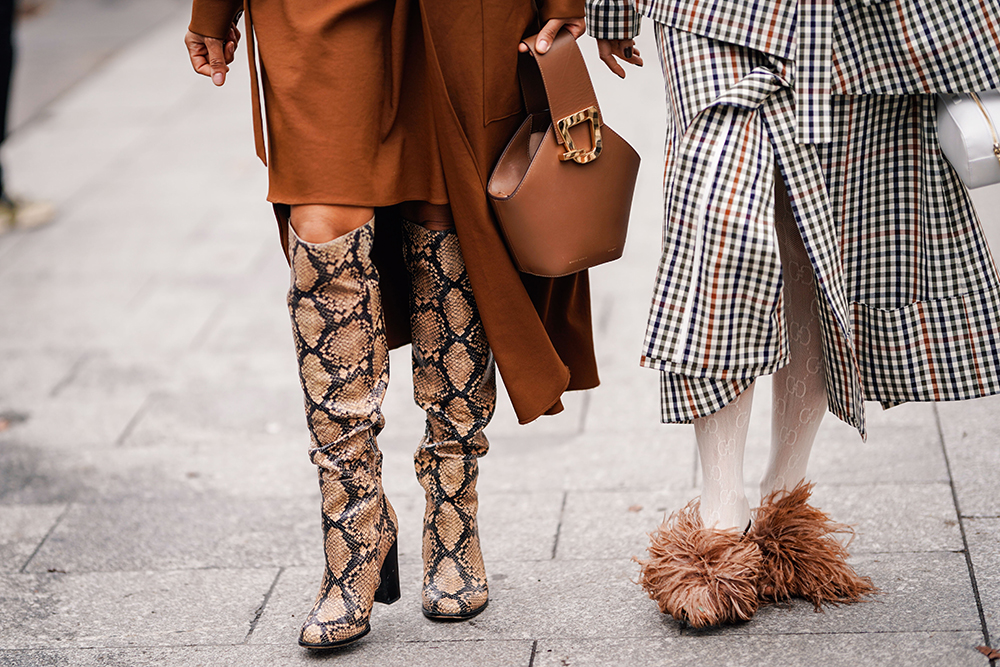 PARIS, FRANCE - MARCH 02: A guest (L) wears a brown dress, a brown Danse Lente bucket handbag, a brown python pattern boots ; a guest a brown and green suit, Gucci tights, brown ostrich feathers decorated shoes, outside Altuzarra, during Paris Fashion Week Womenswear Fall/Winter 2019/2020, on March 02, 2019 in Paris, France. (Photo by Edward Berthelot/Getty Images)