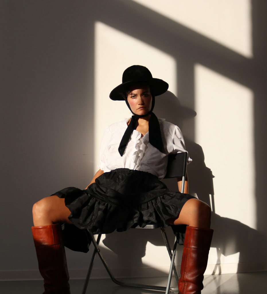 Depop seller Abbey Looker wearing a black hat and skirt, white blouse and knee high brown boots